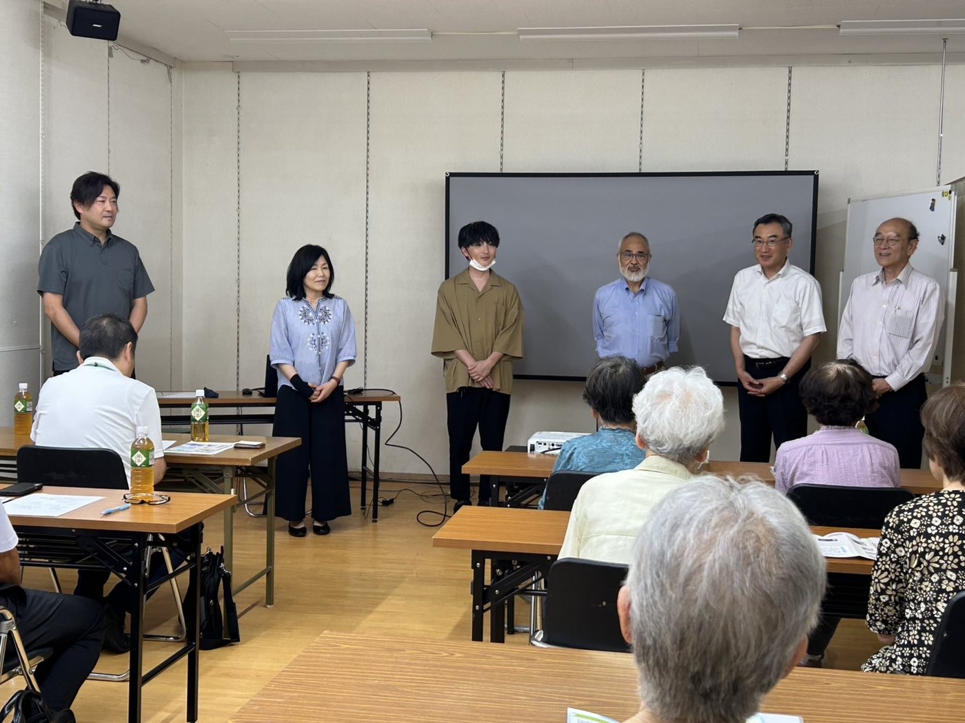 2026年7月23日の生活設計セミナーの写真。会場前方に6人の登壇者が並んで立ち、手前の机で参加者が話を聞いている。